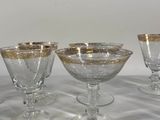 four glass goblets with gold rims are lined up on a table