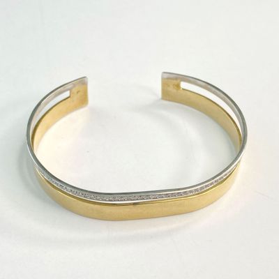 un gros plan d'un bracelet manchette en or et argent posé sur une surface blanche