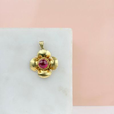 un gros plan d'un pendentif en forme de fleur en or, orné d'une pierre rose en son centre