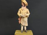 figurine représentant un homme vêtu d'un manteau jaune et d'un chapeau, debout sur une valise