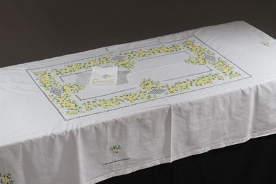 une table recouverte d'une nappe blanche ornée de fleurs jaunes