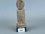 une petite statue en pierre représentant une personne, posée sur un socle