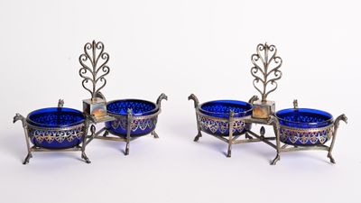 deux plats en verre argenté et bleu posés sur un support, sur une surface blanche