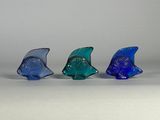 quatre figurines de poissons en verre sont alignées sur une surface blanche