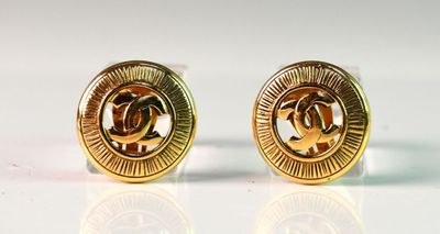 deux paires de boucles d'oreilles Chanel dorées posées sur une surface blanche