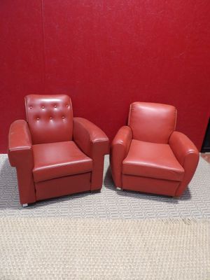 une paire de fauteuils en cuir rouge dans une pièce avec un mur rouge en arrière-plan