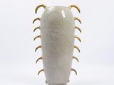 a white vase with gold spiky handles sitting on a white surface