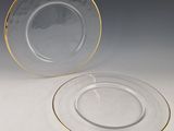 two clear plates with gold rims are sitting on a white surface