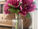un vase en verre contenant des fleurs roses, posé sur une commode