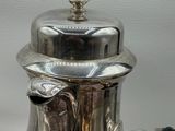 a silver tea pot with a black handle on a table