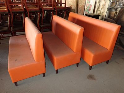trois chaises orange et un banc dans une pièce où l'on aperçoit, à l'arrière-plan, une table et des chaises