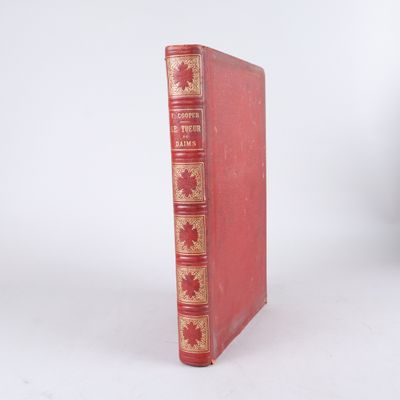 un livre rouge aux tranches dorées posé sur une surface blanche