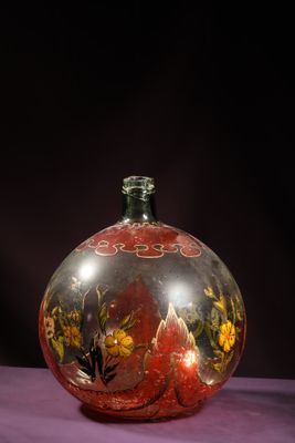a glass vase with flowers painted on it on a purple surface