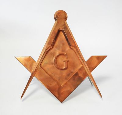 une équerre et un compas maçonniques en cuivre, sur lesquels figure la lettre « g »