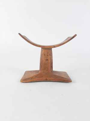 a small wooden stool with a curved seat on a white surface