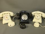 three old fashioned telephones are lined up on a gray surface