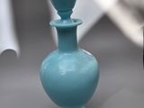 a small blue vase sitting on a table next to a cell phone