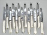 six silverplated knives and six knives on a white surface