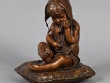 an antique bronze figurine of a child sitting on a pillow
