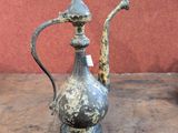 a silver tea pot sitting on a table with a red wall in the background