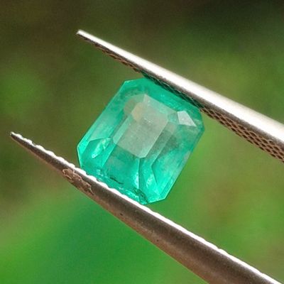 un gros plan d'une émeraude verte tenue par une paire de pinces