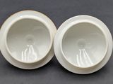 pair of white porcelain bowls with gold rims sitting on a table