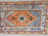 an orange and blue rug hanging on a wall next to a white wall