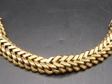 a gold necklace with a braid design on a black surface