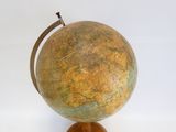un petit globe posé sur un socle en bois, lui-même posé sur une surface blanche