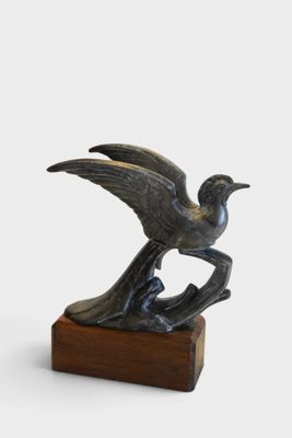 bronze sculpture of a bird on a wooden base on a white background