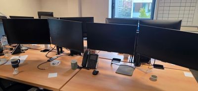 trois écrans d'ordinateur posés sur le bureau, avec un téléphone