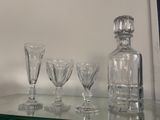Des bouteilles et des verres sont posés sur une étagère en verre devant un mur blanc.