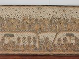 a tapestry on display in a museum with a wooden stand