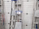 Plusieurs échelles sont alignées contre un mur blanc dans un entrepôt
