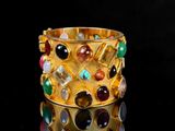 gold plated bracelet with multi colored stones on a black surface