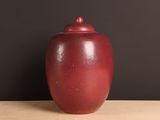 un vase rouge posé sur une table, avec un mur noir en arrière-plan