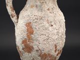 un vase blanc et marron muni d'une anse, posé sur un socle noir
