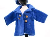 une poupée vêtue d'un manteau bleu et d'un chapeau, posée sur un mannequin