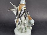 a figurine of a woman sitting on a tree branch with two birds