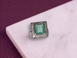 une image représentant une bague sertie d'une pierre verte posée sur une surface en marbre blanc