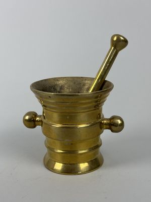 un mortier et un pilon anciens en laiton sur fond blanc