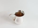 an antique silver pitcher with a handle on a white surface
