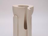 un vase blanc percé d'un trou, posé sur une surface blanche
