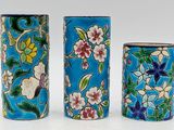 three blue vases with flowers on them on a white surface