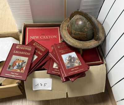 Des cartons remplis de livres et un globe terrestre sont posés par terre devant un mur