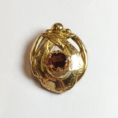 une image représentant une broche de couleur dorée ornée d'un grenat au centre
