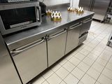 un plan de travail en acier inoxydable dans une cuisine professionnelle, sur lequel est posé un micro-ondes
