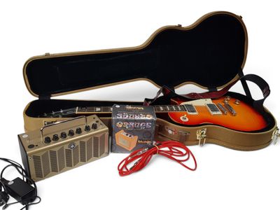 une guitare, un amplificateur et un étui à guitare posés sur une surface blanche