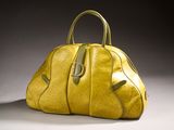 yellow leather handbag sitting on a white surface with a gray background