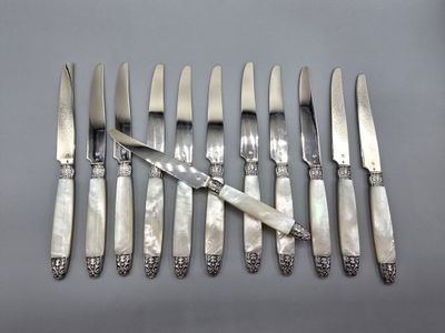 un service de huit couteaux en métal argenté et un couteau posé sur une table